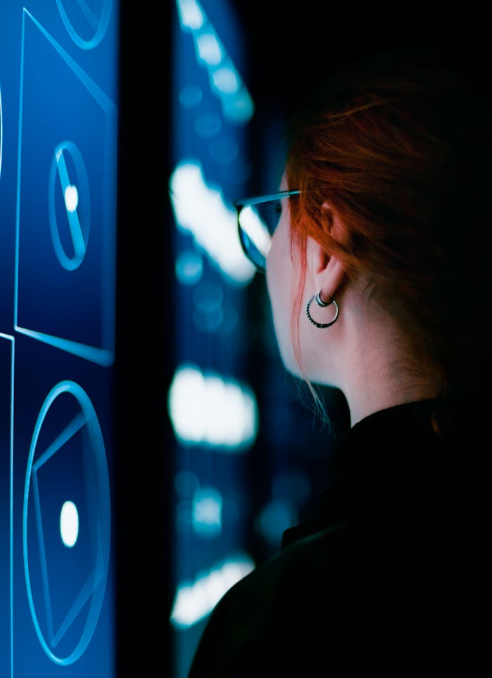 A woman with eyeglasses interacts with an illuminated digital screen, showcasing modern technology.